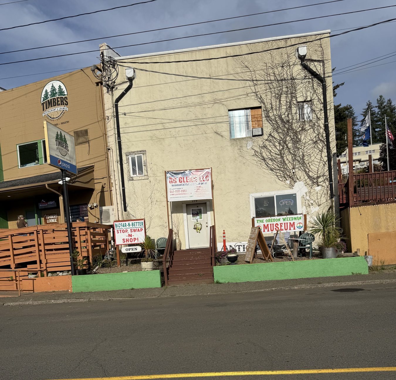 The shop from SE Butler Bridge Road, next to Timbers Restaurant & Lounge, with the Biggar-N-Better sign on the green curb.